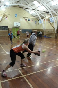 A lady covering third base scoops up the ball as it's hit into play.